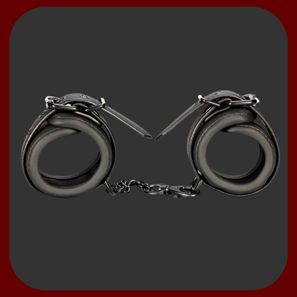 Nastavitelné BDSM pouta z černé veganské ekokůže s kovovým řetízkem bez niklu. Vhodné pro použití na zápěstí i kotníky, s polstrovaným vnitřkem pro pohodlné nošení.